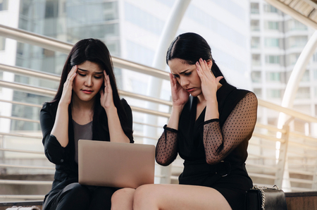 two young beautiful business woman feeling tired and stressed with laptop computer having problems with project and sitting on stairs in modern city, investment, financial, working and emotion conceptの写真素材