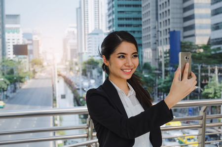 young asian business woman smiling wearing modern black suit video conference with mobile phone in building city background, network technology, internet, digital financial and investment conceptの写真素材
