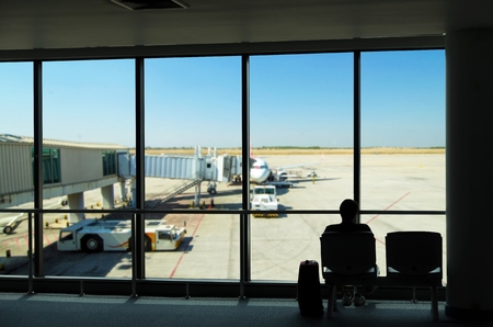 silhouette of business tourist people with luggage looking at airplanes and waiting at the plane boarding gates before departure in airport, travel, lifestyle and transportationの写真素材