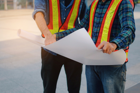midsection of engineer, technician or architect with safety helmet planning about building plan with blueprint in city building background, construction site, business, industry and worker conceptの写真素材
