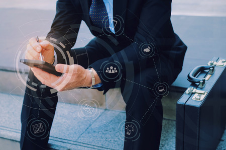 hand of business man wearing modern black suit using mobile smart phone and briefcase sitting on...