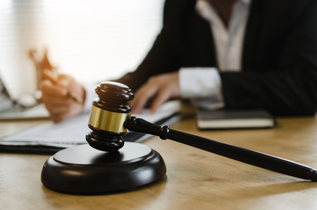 justice lawyer in black suit working about legal legislation with documents on workplace desk in courtroom office behind wooden judge gavel, occupation, business, justice law and legal service conceptの写真素材