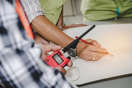 engineer or technician holding red walkie talkie and planning about building plan with blueprint and construction tools on conference table at construction site, industry, construction conceptの写真素材