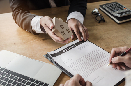 real estate broker manager giving wooden house model to customer after signing contract for buying house in estate agent office, investment, home loan contract, buying house, real estate conceptの写真素材
