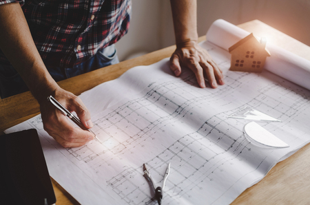 professional architect, engineer or interior in plaid shirt reviewing blueprint on workplace desk at home office, construction, engineering, industry, contractor and business concept, vintage toneの写真素材