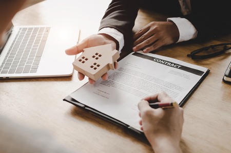 real estate broker manager giving wooden house model to customer after signing contract for buying house in estate agent office, investment, home loan contract, buying house, real estate conceptの写真素材