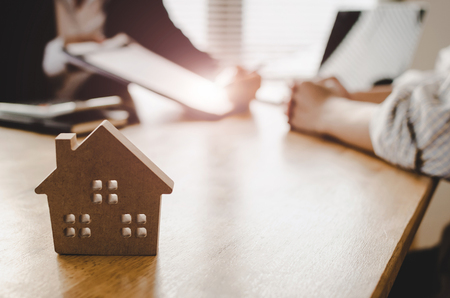 customer signing contract for buying house with real estate broker in estate agent office behind wooden house model, investment, home loan contract, real estate, insurance, buy and sell house conceptの写真素材