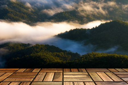 empty brown wooden floor or modern board, terrace with soft focus image of beautiful view sunrise of mountain with morning mist in Thailand, travel, landscape and nature concept with copy spaceの写真素材