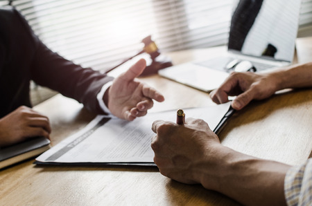 client customer signing contract and discussing business with legal consultants, notary or justice lawyer with laptop computer and wooden judge gavel on desk in courtroom office, legal service conceptの写真素材