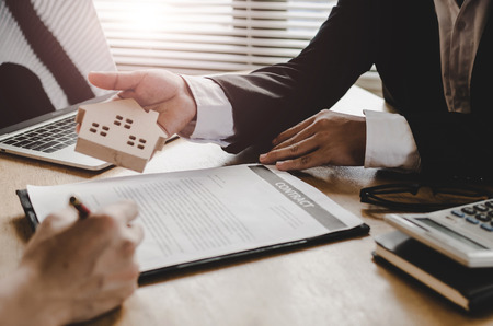 real estate broker manager giving wooden house model to customer after signing contract for buying house in estate agent office, investment, home loan contract, buying house, real estate conceptの写真素材