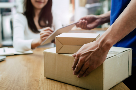home delivery service man in blue uniform and young woman customer appending signature in digital mobile phone receiving parcel post box from courier at home, express delivery, online shopping conceptの写真素材