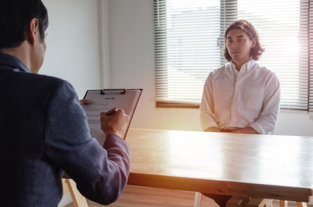 young attractive man during job interview and explaining about his profile with business HR manager holding resume and sitting in meeting room at office, business job interview and employment conceptの写真素材