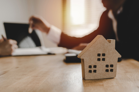 close up House model with real estate broker manager giving keys to customer after sign contract for buying house in estate agent office in background, home loan contract, buy and sell house conceptの写真素材