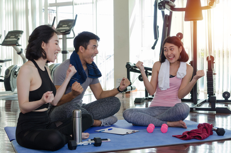 group of young sporty people cheer up and laughing together sitting on yoga mat in fitness gym after workout, exercise at morning, encouragement, training, partnership, success and teamwork conceptの写真素材