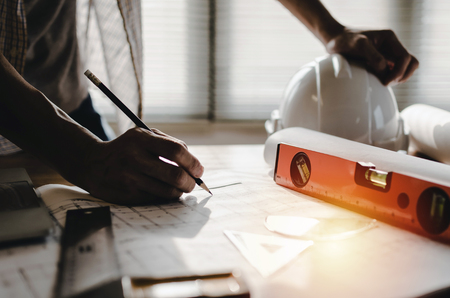 professional architect, engineer or interior drawing on blueprint with white safety helmet on workplace desk in office center at construction site, contractor, construction, engineering conceptの写真素材