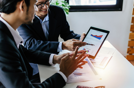 young partner business man investor talking about financial statistics chart information in mobile tablet together sitting in meeting room at office, finance, investment and digital technology conceptの写真素材