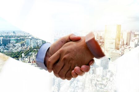 Partnership. double exposure image of investor business man handshake with partner for successful meeting deal with during sunrise and cityscape background, investment, partnership, teamwork conceptの写真素材