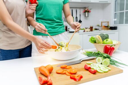 Diet. two young pretty woman in green and brown shirt preparing the vegetables salad in bowl for good healthy in modern kitchen at home, healthy lifestyle, cooking, healthy food and dieting conceptの写真素材