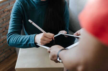 woman customer get a pen form delivery service man in red uniform for signature in digital mobile tablet receiving parcel post box from courier at home, express delivery and shopping online conceptの写真素材