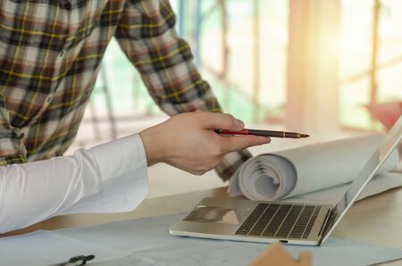 project manager pointing with pen on laptop computer with construction worker team and blueprint on desk during discussing planing for new project at construction site, contractor, engineering conceptの写真素材