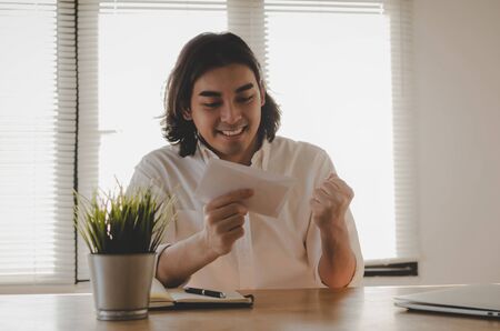 happy young asian employee business man holding money bonus card in paper envelope to increasing of salary or promotion new position in office, new job celebrate salary and resignation letter conceptの写真素材