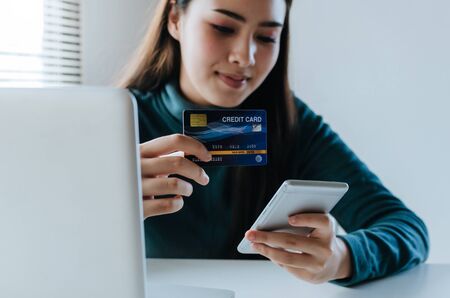 young pretty woman using mobile smart phone for scan and pay online bills on desk in home office, plan money cost saving, investment, business finance, expenses, payment and shopping online conceptの写真素材