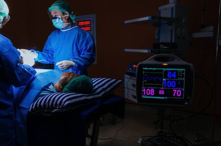 medical team surgeon performing surgery at work with with ECG/EKG monitor showing heart rate for...