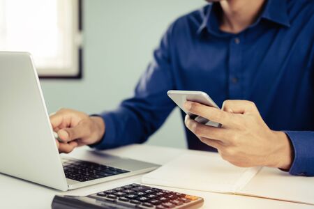 business man in blue shirt using mobile phone working with laptop computer and document report on...