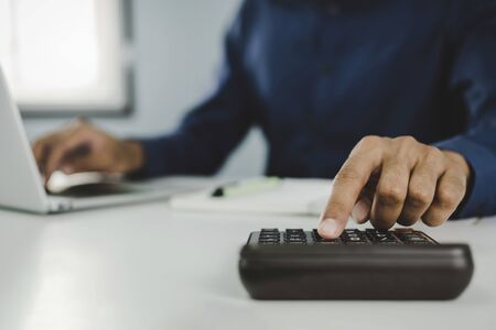 hand of business man in blue shirt calculate about financial with calculator and working on laptop computer and report on desk at home office, work from home, business finance and accountant conceptの写真素材