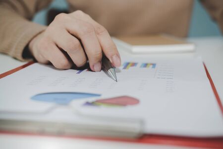 business woman working and calculating about finance with strategy graph chart, document report and notebook on desk at home, work from home, digital online marketing and financial business conceptの写真素材