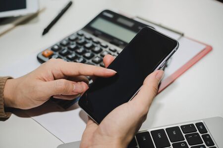 young woman using digital mobile phone working and calculate about finance information on desk at...