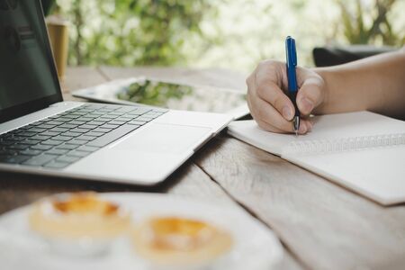 man relaxed writing and working with digital laptop computer with egg tart dessert on desk at cafe...