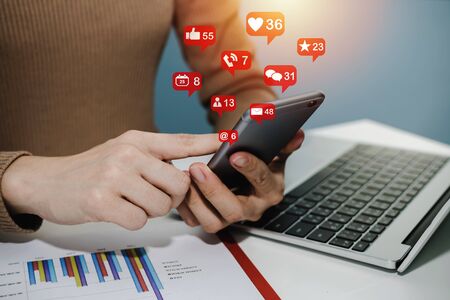 hand using social network on digital mobile phone with virtual icon, laptop computer and report on desk at home office, digital marketing, work from home, business finance, network technology conceptの写真素材