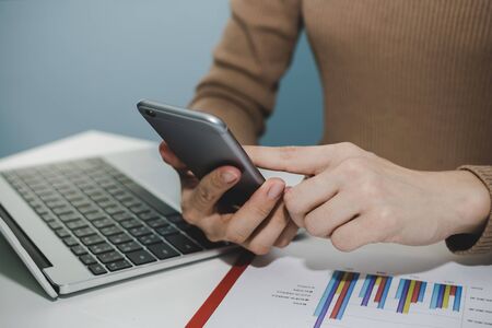 woman working about financial on digital mobile phone, laptop computer and graph chart report on desk at home office, digital marketing, strategy, work from home, business finance technology conceptの写真素材