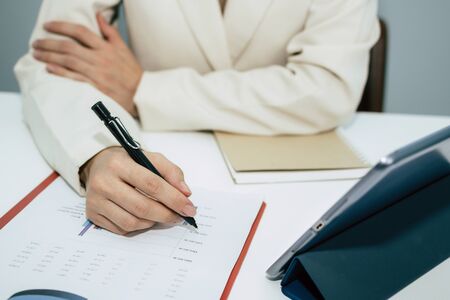 attractive businesswoman in white suit working and calculating about finance with, document report and digital mobile tablet on desk at office, digital online marketing and financial business conceptの写真素材