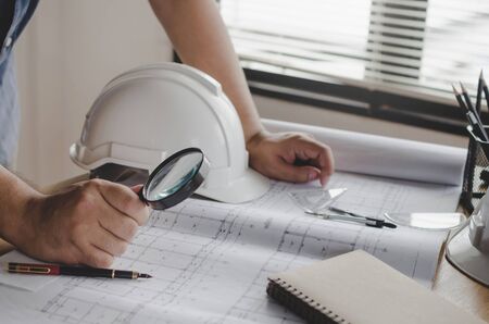 hands engineer or architect working on blueprint and white safety helmet on workplace desk in meeting room project at construction site office, contractor, engineering and construction conceptの写真素材