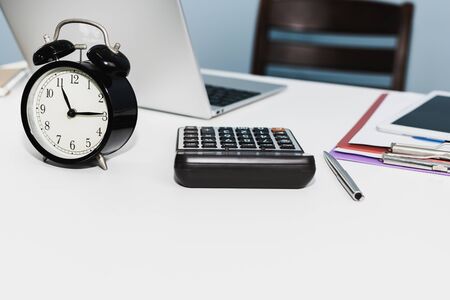 retro style black alarm clock with digital laptop computer, calculator, digital mobile tablet and document report on white desk at home office, night working late, business finance, object conceptの写真素材