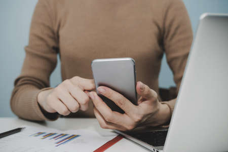 businesswoman hand working with digital mobile smartphone, laptop computer and report on desk at...