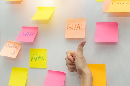 Goal. business woman showing thumbs up with colored sheets sticky note paper on white board background in office, business meeting, brainstorming, creative, digital online marketing, financial conceptの写真素材