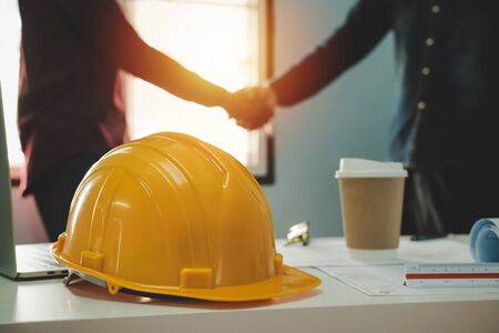 Contractor. yellow safety helmet on workplace desk with construction worker team hands shaking greeting start up plan new project contract in office center at construction site, partnership conceptの写真素材