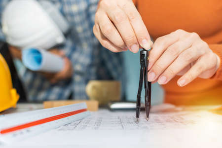 professional architect and interior designer hands drawing with divider compass on blueprint on desk in meeting room office at construction site, construction industrial, engineering business conceptの写真素材