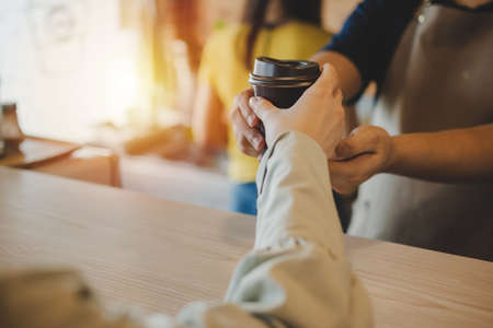 hand of friendly barista serving hot coffee cup to happy female customer over counter in modern cafe coffee shop, cafe restaurant, service mind, hot coffee ,small business owner food and drink conceptの写真素材