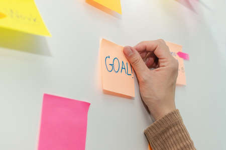 Goal. business woman hand with colored sheets sticky note paper on white board background in office, business meeting, brainstorming, creative, digital online marketing, business financial conceptの写真素材