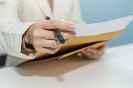 attractive businesswoman in white suit hand open business report from document envelope and working on desk in meeting room at home office, digital online marketing and financial business conceptの写真素材