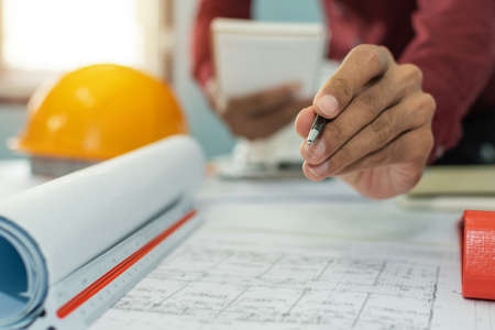 hand interior designer, engineer or architect drawing on blueprint with safety helmet in meeting room at construction site office, interior design, contractor, engineering and construction conceptの写真素材