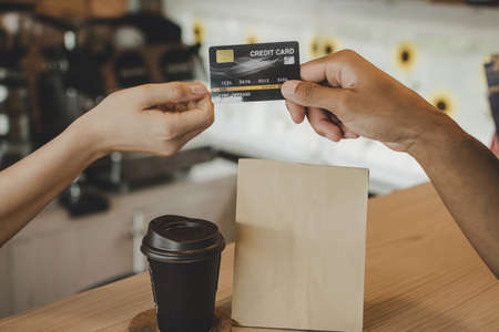 hand customer paying with credit card for buying hot coffee cup on counter in modern cafe coffee shop, cafe restaurant, digital payment, small business owner, takeaway food, food and drink conceptの写真素材