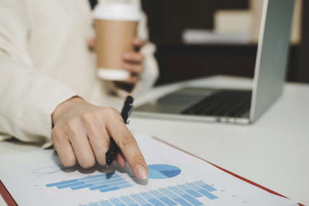 attractive businesswoman in white suit drinking coffee and working calculate about finance with,...