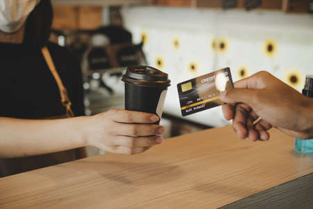 hand customer paying with credit card for buying hot coffee cup on counter in modern cafe coffee shop, cafe restaurant, digital payment, small business owner, takeaway food, food and drink conceptの写真素材