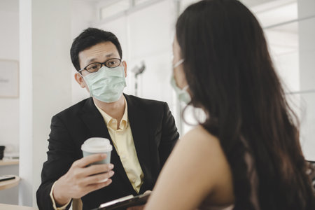 Businessman wearing protection face having friendly conversation and drinking coffee while break time with friend, new normal, virus prevention, social distancing conceptの写真素材