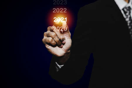 Goal target. businessman hand touching and pointing with pen on year 2021 with virtual screening on dark background, change from 2010 to 2021, strategy, business planning and happy new year conceptの写真素材